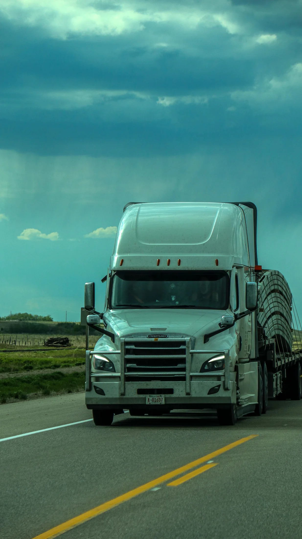 White semi-truck traveling on an open road beneath a broad sky
